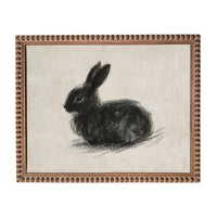 A black rabbit sitting on a beige background, framed in a brown frame.